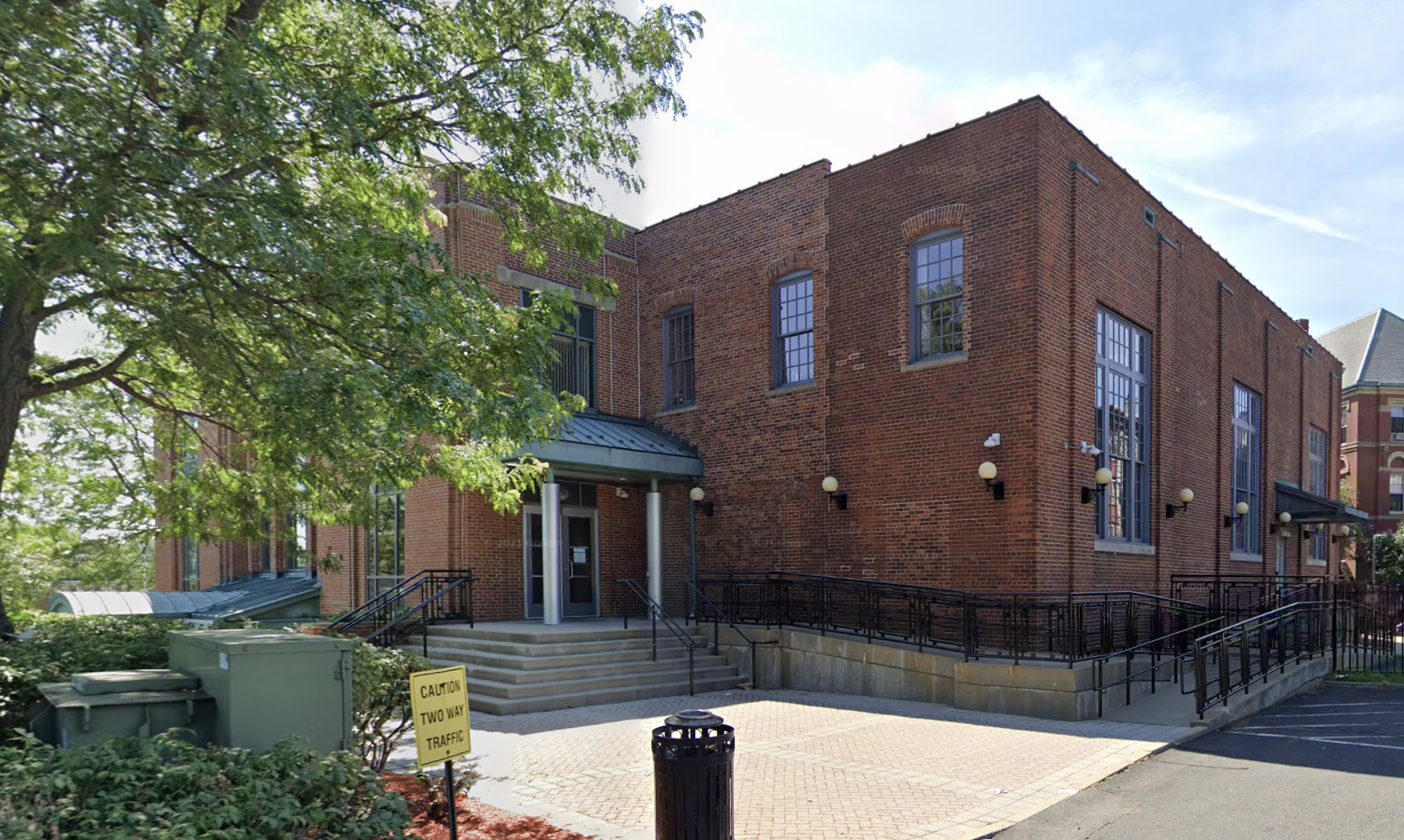 A 2-story brick building surrounded by trees and a small brick courtyard. A parking lot can be partially seen in the foreground.