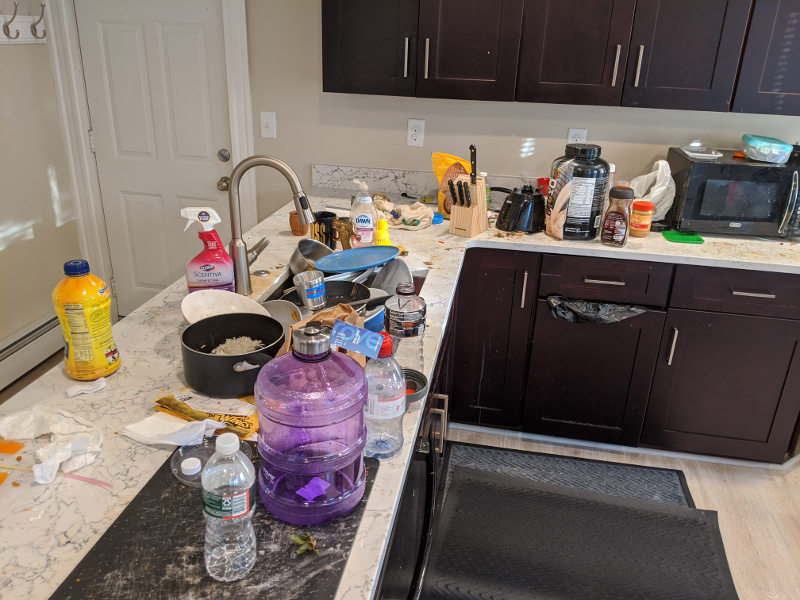 A recently renovated kitchen is covered in culinary detritus. The sink is full and unusable.
