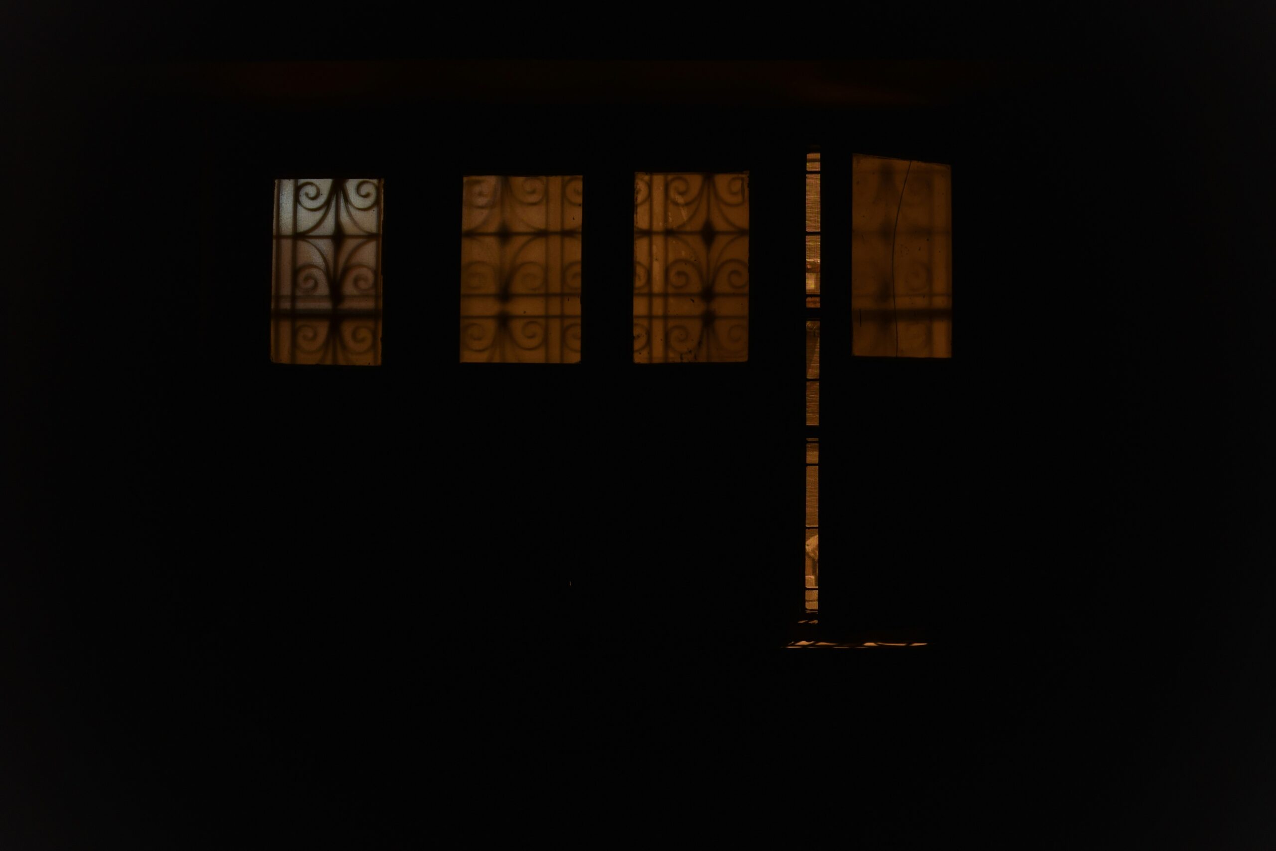 a backlit door with metal details over glass, with matching windows to the left. The door is ajar showing a crack of the lit interior.