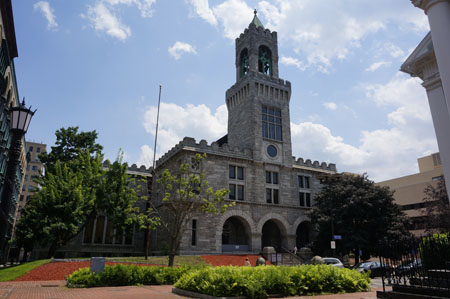 The exterior of the Springfield Juvenile/Housing Court, a tall building made of stone, with a brick courtyard and some bushes out front.