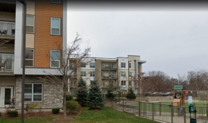 A street view of a luxury apartment complex made of stone, siding and contemporary materials, with playground structure in the foreground.