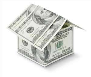Hundred dollar bills have been folded and stacked to create the shape of a simple square house with peaked roof.