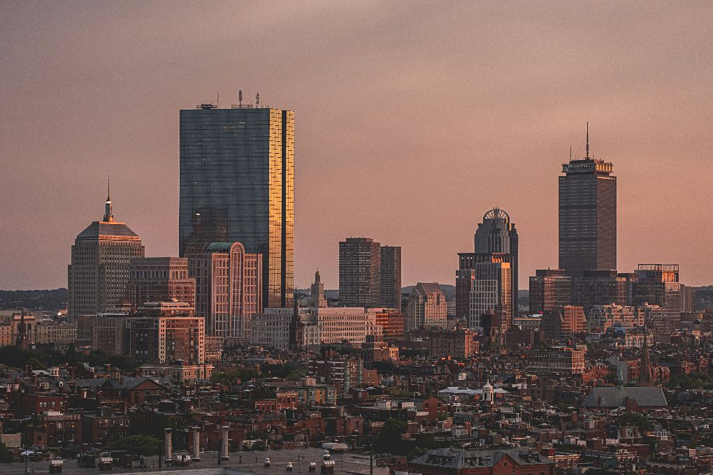 The Boston skyline from a distance looks hazy at sunset.