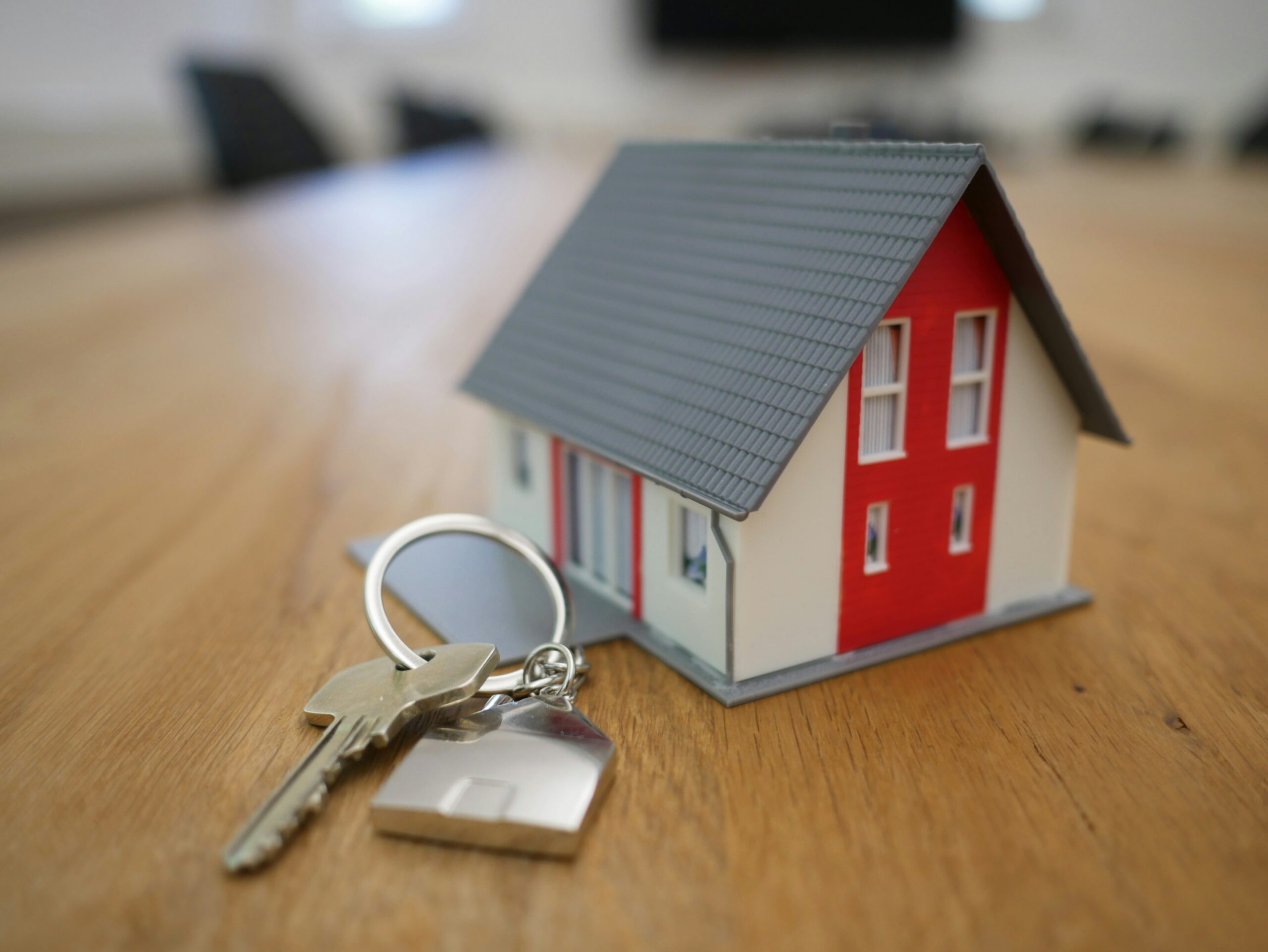 An image of a miniature red and white house sitting on a tabletop, with a house key next to it.