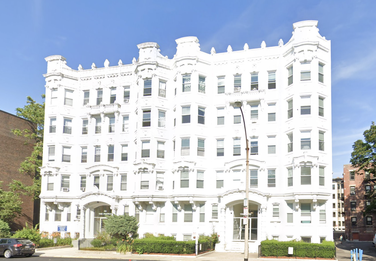 A street view of 80 The Fenway, a collection of condos and apartments in a white multistory stone building. The building has two front entrances, each labeled “80 The Fenway,” and is on what appears to be the end of a roundabout or cul de sac.