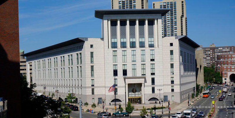 A view of the exterior façade of the Edward Brooke courthouse, a tall multi-story white stone building with columns above the top row of windows on the front.