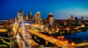 an aerial view of Boston at night, with buildings and bridges lit up against a dark blue sky.