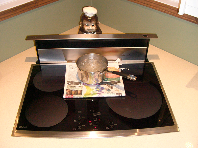 An induction countertop model stove brings water in a pan to a rolling boil. A piece of newspaper sits between the stovetop and the pan.