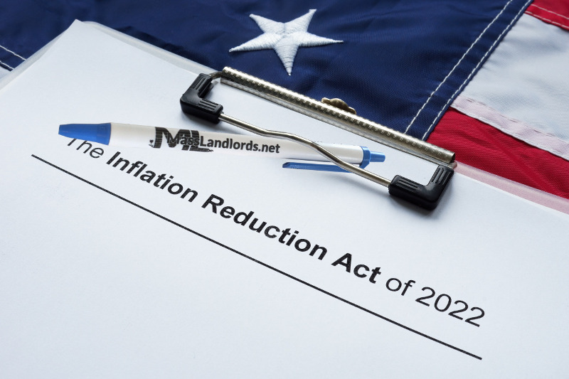 MassLandlords has parsed the Inflation Reduction Act of 2022 for you. An American flag draped across a desk is partially covered by a clipboard on which is a MassLandlords pen and the cover page of the Inflation Reduction Act of 2022.