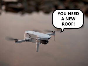 A white drone with camera flies against a blurred background. A white cartoon speech bubble reads “You need a new roof!”