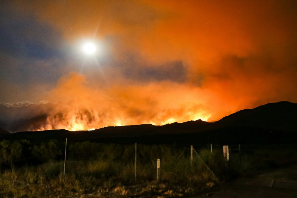 A raging wildfire behind a hilly area of California nearly blocks out the sun with large clouds of smoke.