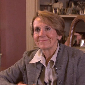 Jane wears a bob cut hairstyle, collared shirt with wide lapels and a button-down sweater jacket.