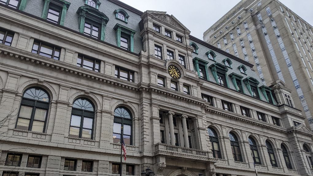 A street-level view of the John Adams Courthouse, a multistory, long building made of stone.