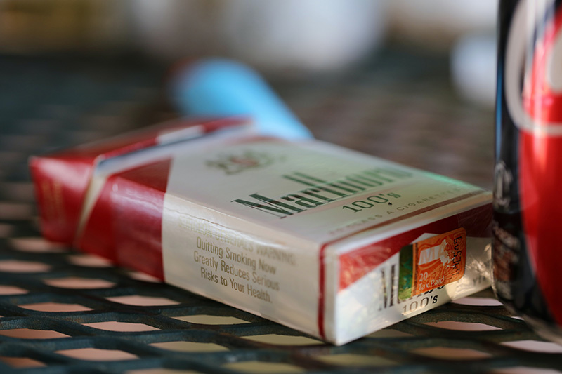 A red and white pack of cigarettes is lying on its back in a dimly lit environment, with the edge of a soda can visible on the right.