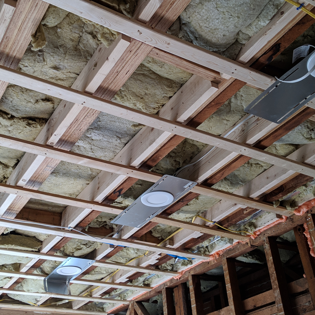 A ceiling has been opened to reveal the joists of the floor above. Strapping runs perpendicular to the joists for the sheetrock ceiling to be installed. Above all of this are coarse looking bats of soundproofing material.