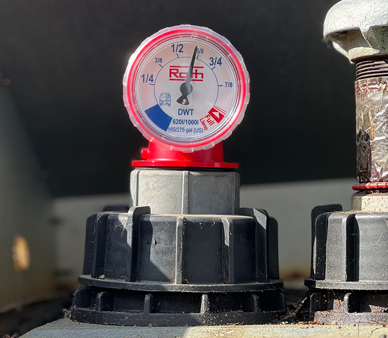 A close-up of a red and white Roth oil tank fuel gauge, showing the tank is approximately 5/8 full.