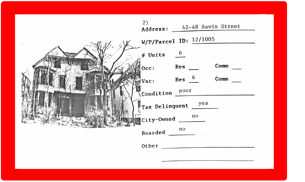 A computer scan of a black and white photo of boarded up, abandoned building, with an identification field to its right, on a red background.