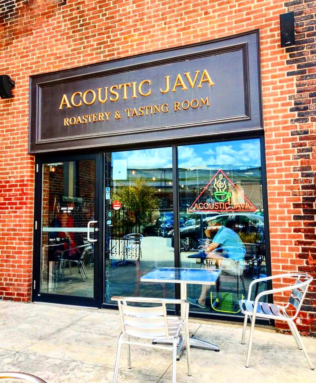 The glass front of Acoustic Java shows a brick building with outside seating.