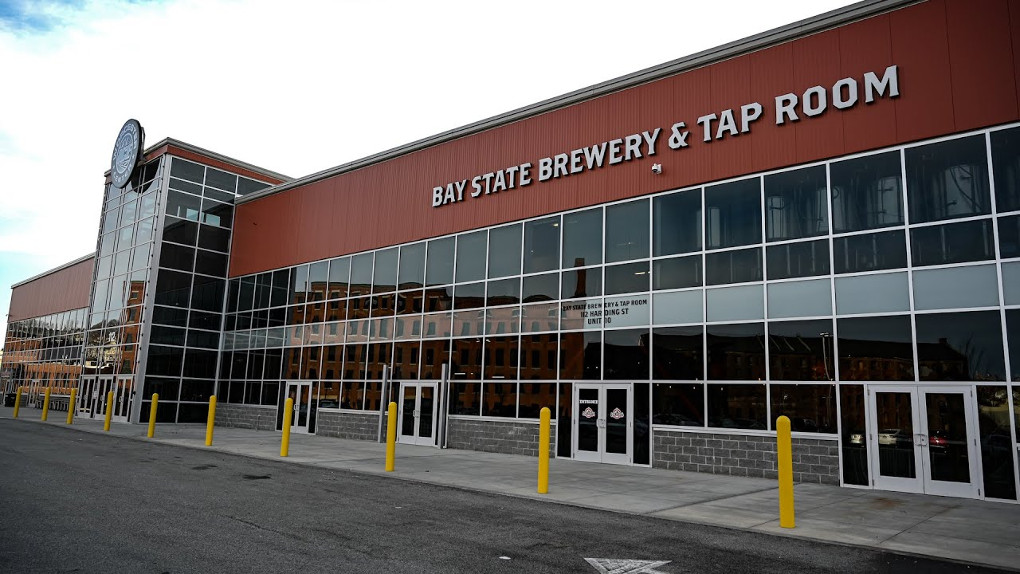 The glass front of Bay State Brewery shows a recently built building alongside a large parking lot.