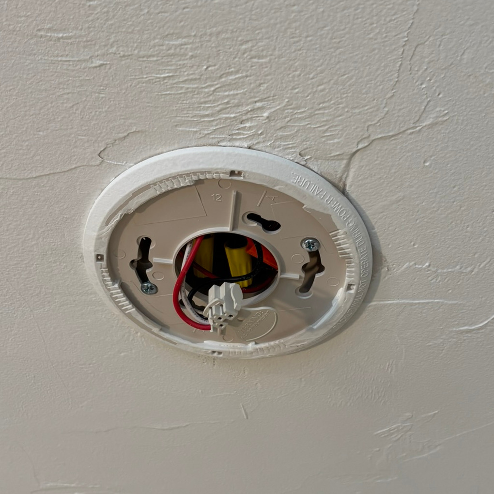 A smoke alarm bracket shows where a smoke detector used to be installed. Disconnected wires are visible hanging from the ceiling.