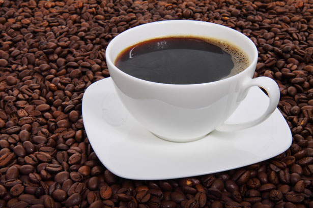 A ceramic coffee cup and saucer sits on a bed of roasted coffee beans.