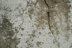 A close-up photograph of a concrete wall with a spiderweb network of cracks, some of which go deep into the stone.