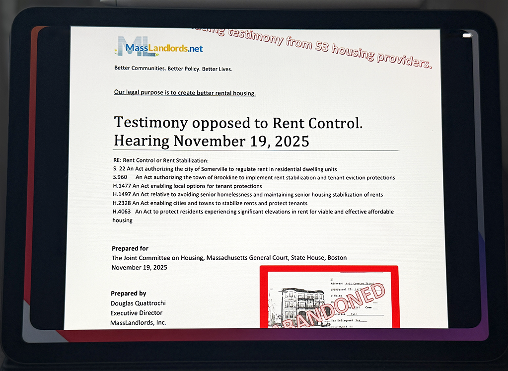 A composite image of an iPad screen with dark border. The page on the screen is a partial view of the first page of anti-rent control testimony. The MassLandlords logo is visible, along with a partial photograph of a rundown building stamped “abandoned.”