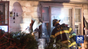 A fire fighter investigates the base of a building with vinyl siding melted and warped by fire.