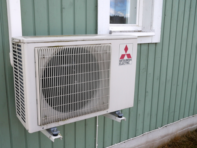 A Mitsubishi electric heat pump unit attached to the exterior of a wood frame building.