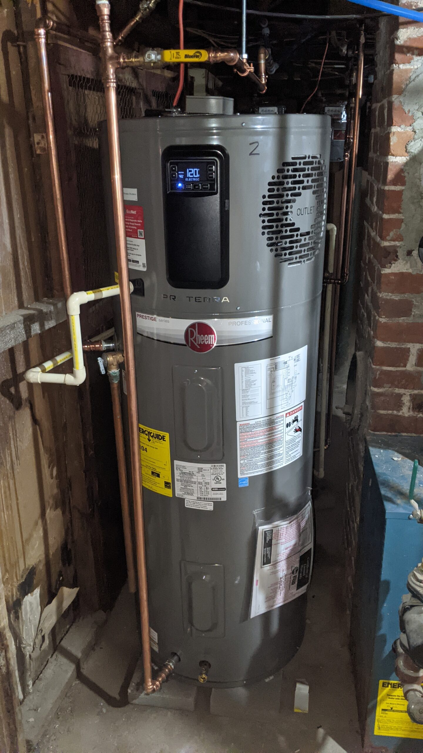A tall heat pump water heater sits beside a chimney. There is no exhaust pipe coming out of it. A panel with buttons beeps when pressed to raise or lower the water temperature.