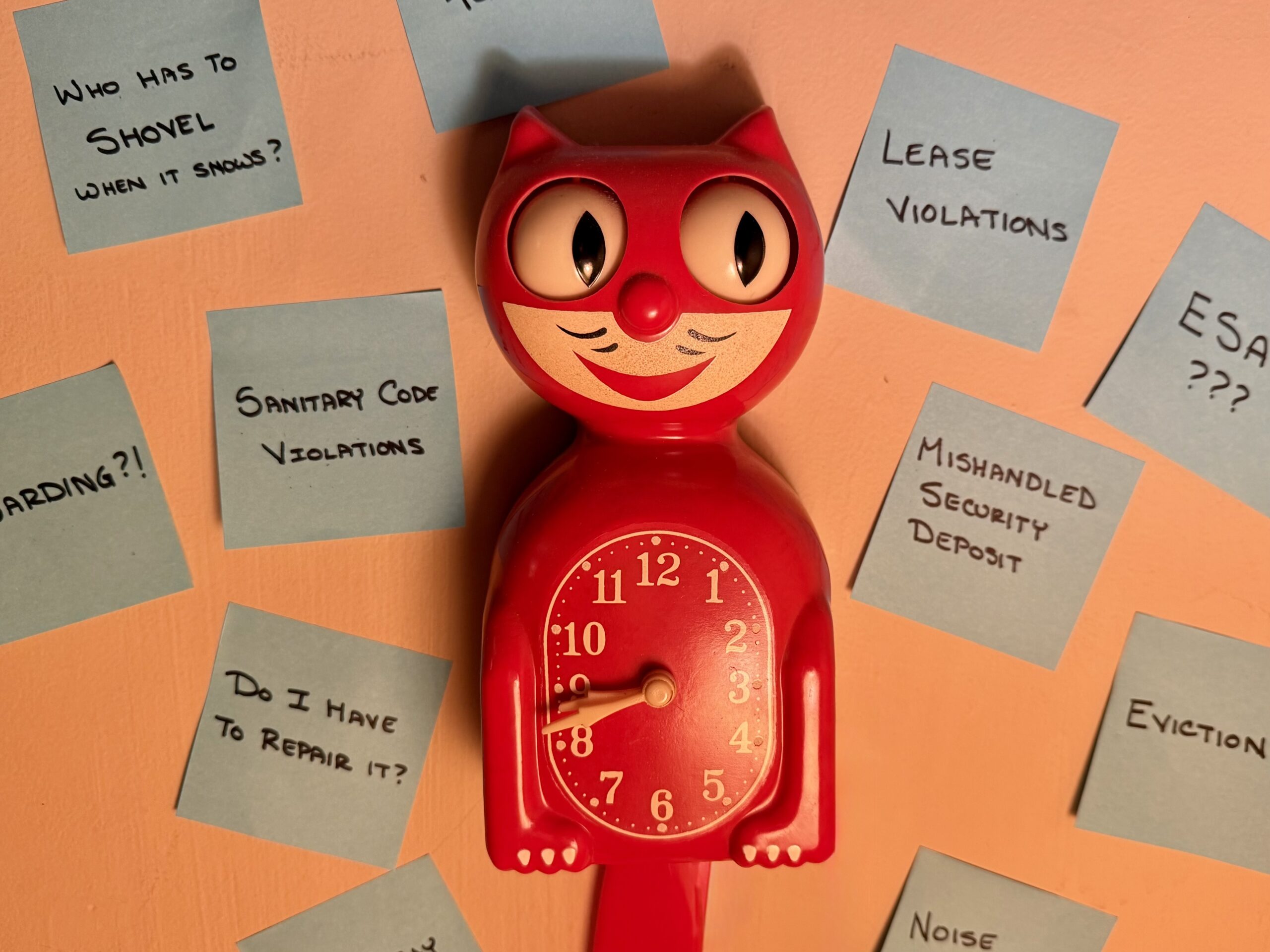 An old fashioned red cat clock sits on a beige wall. Blue Post-It notes surround the cat with statements such as “Security Deposit Violation” and “ESA?” in block letters, representing landlord concerns.