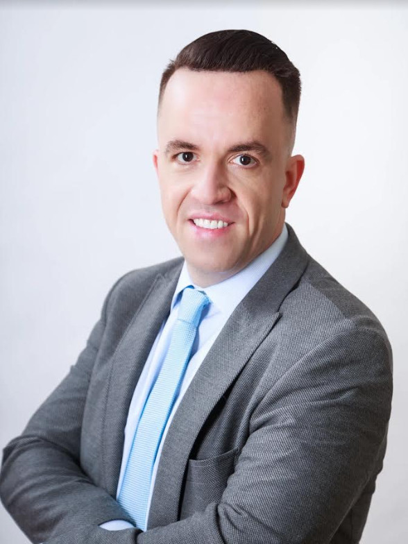 Attorney Craig Higgins wears a suit, tie and close cropped hair and smiles.