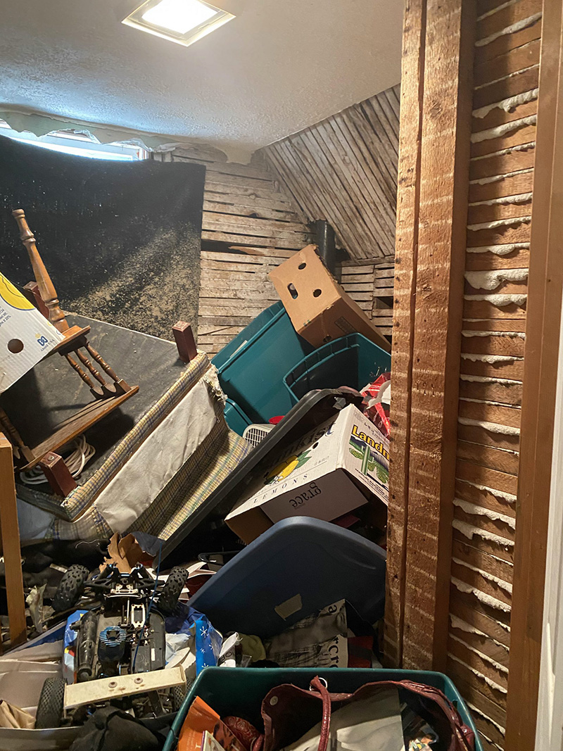 A room with no drywall (only wall slats) is full almost to the ceiling with boxes and other debris and trash.