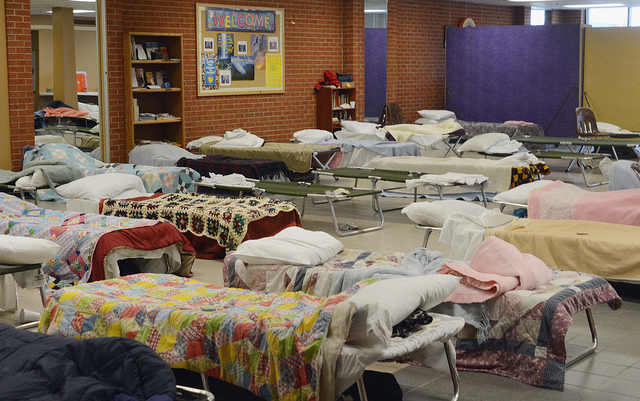 A representative temporary shelter with cots, but with donated blankets and quilts. The average stay in shelter in MA is ten months. Insurance Against Homelessness promises to shorten this average stay by 45 days at least. (CC-BY KOMU News Missouri)