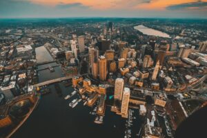 an aerial view photograph of Boston shows many high-rise buildings, the river, and seaport, and the communities beyond.