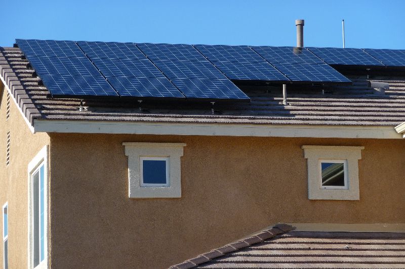 A close up photo of a small array of solar panels on the roof of a stucco house on a sunny day.