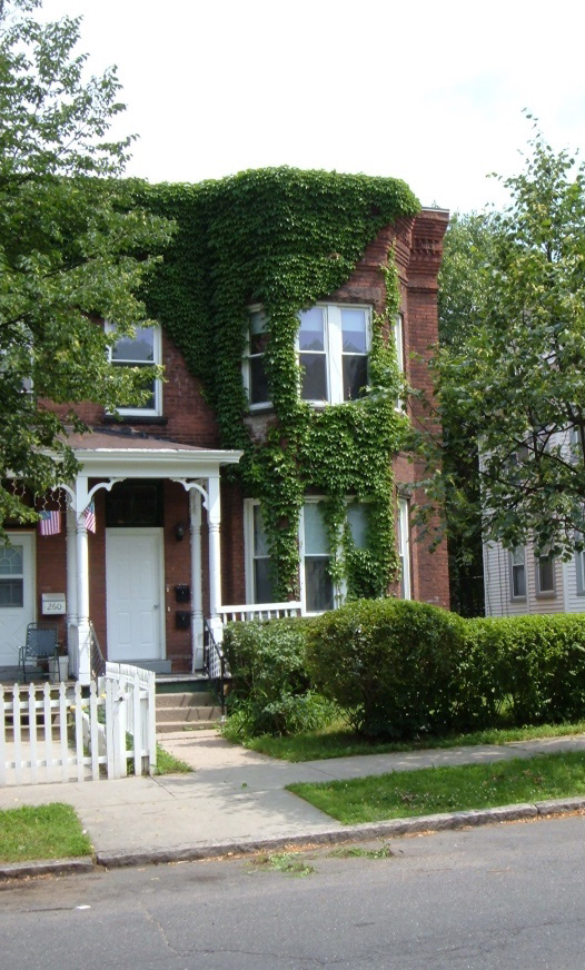 photo of a historic multifamily home in Holyoke, Mass., a brick two-story building with white picket fence and ivy growing up the exterior.