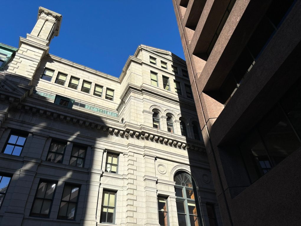 Low winter sunlight shines on an ornate, late 19th century concrete structure. A modern steel skyscraper in shadow sits to the right of the building.