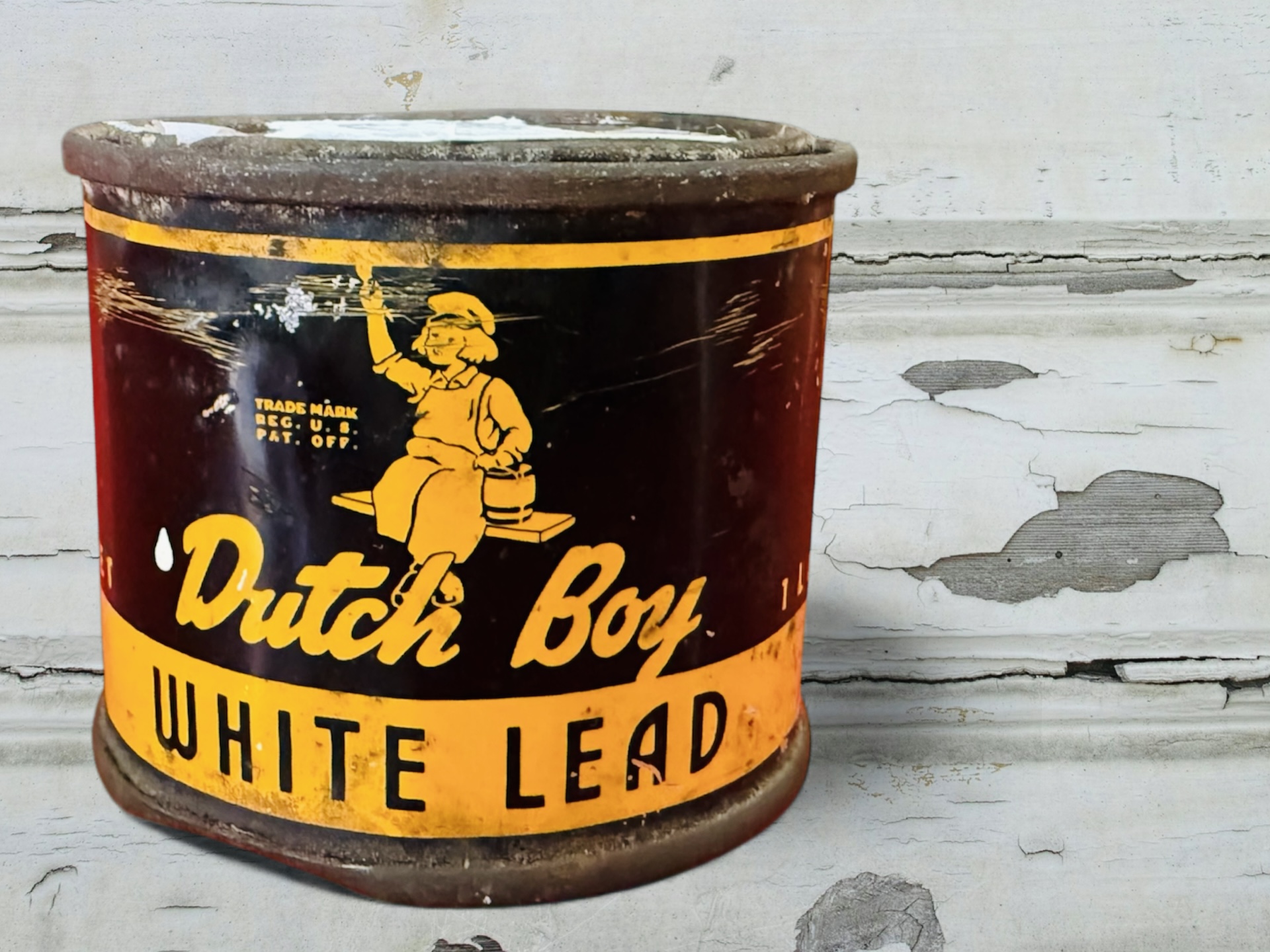 A small dented can of Dutch Boy white lead paint sits in front of a background of wooden boards with peeling white paint.