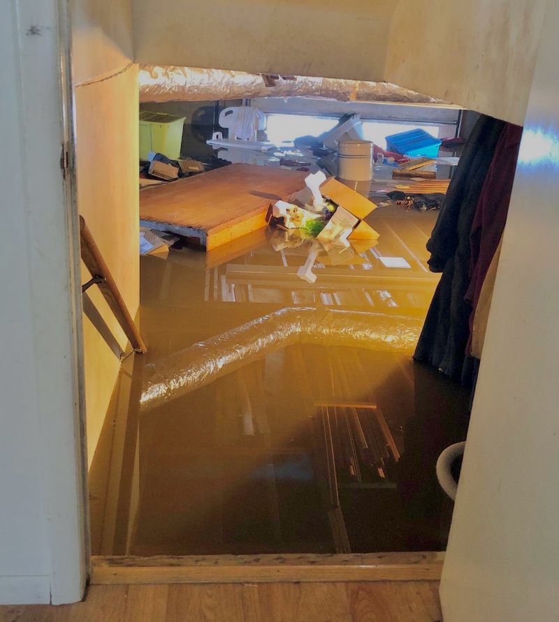 photo of a flooded basement with items floating in the brown water, which reflects an insulated duct and other items above the water.