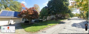 google image of a sunny, tree-lined street in the Belvidere section of Lowell, Mass., showing a handsome home with large yard and solar panels in the foreground, and down the street with similar homes lining each side.