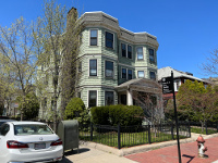 A view of Petrillo Square. A three decker with apparently six units (two vertical stacks of bay windows letting in warm sun) face the marker put in place to honor Peter and Helen Petrillo. The street address is Magazine and Chestnut, Cambridge, Mass.