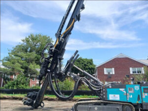 Photo of a large underground drill poised to penetrate ground on a clear, sunny day with wispy clouds in the sky.