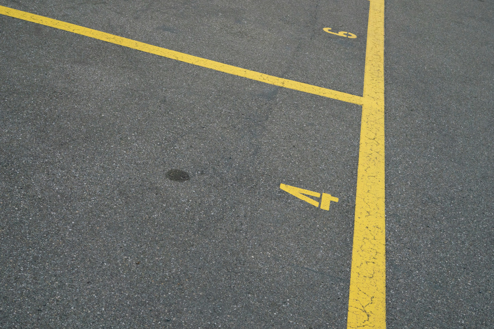 A close-up of pavement shows parking spaces indicated by yellow lines with yellow numbers. Spaces number 4 and 6 are visible. Licensed Claudio Schwarz for Unsplash.