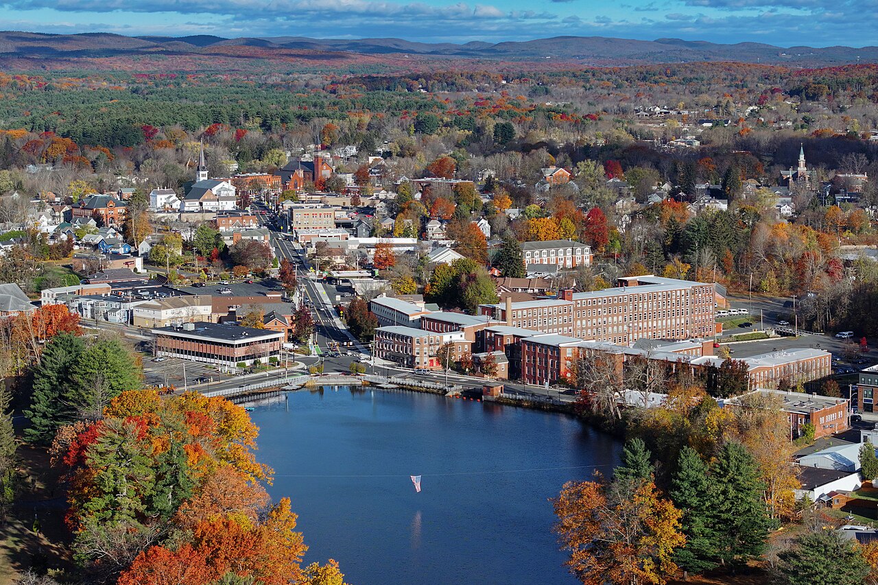 A drone aerial view of Easthampton, Massachusetts, shows a large body of water, mills, and homes and forest in the distance.