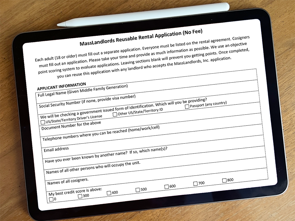 An iPad sits on a wooden desk. The iPad shows the MassLandlords rental application. The first few fields are on-screen.