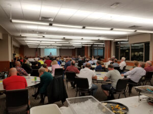 Worcester event attendees sit gathered around tables of eight listening to a speaker at the front of the room. Dinner has been served.