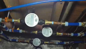 A photo of three water meters connected to brass piping, each displaying numbers of water usage readings that are not clear or easy to read.