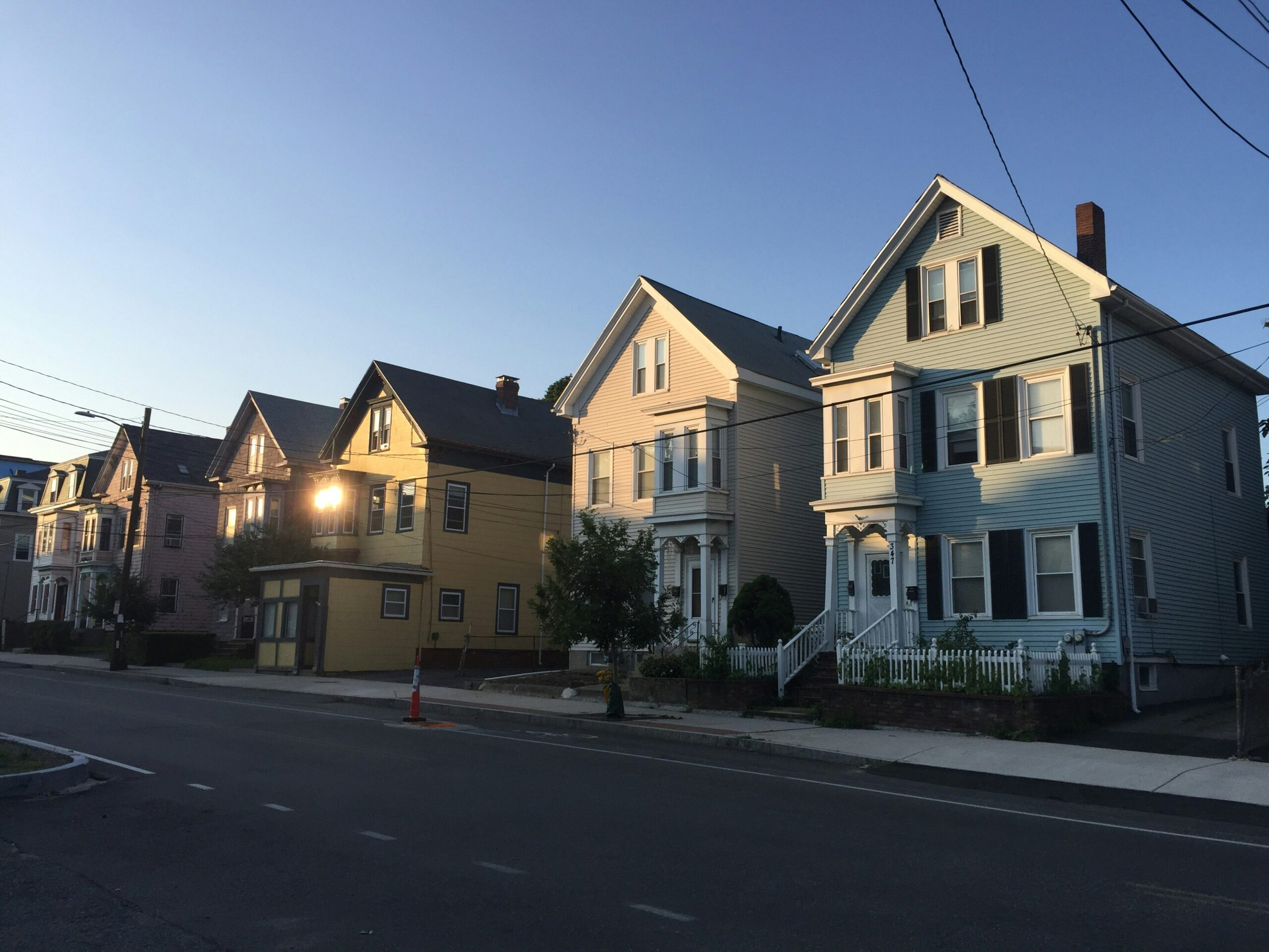 A photograph of Beacon Hill in Somerville at sunrise, where multiple multifamily homes sit very close together, and quite close to the sidewalk.