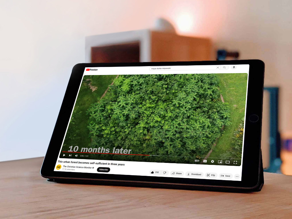 An ipad sits on a table showing YouTube Premium open to a video by the Christian Science Monitor. The video title is 'This urban forest becomes self-sufficient in three years."